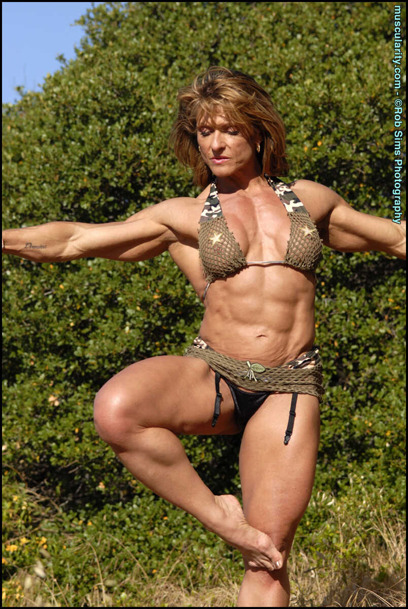 Middle-aged bodybuilder Emery Miller strips off her bikini in the shade of mature trees, revealing her muscular physique a...