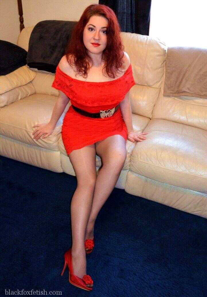 Redheaded MILF in Red Dress and Heels Poses on Leather Sofa with a Seductive Smile - Mada Rose