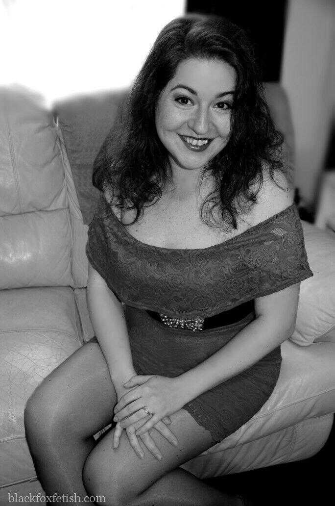 Redheaded MILF in Red Dress and Heels Poses on Leather Sofa with a Seductive Smile - Mada Rose