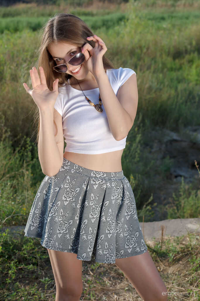 Long haired teen Hrizantema strips to her sneakers by a tree in a field and bends over for the camera to show off her tigh...