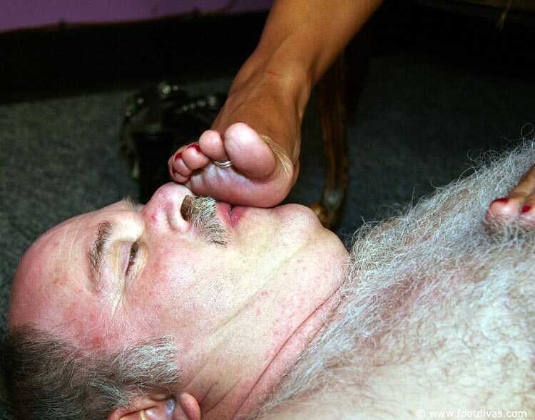 Caucasian female rubs her feet all over an old man's face - 