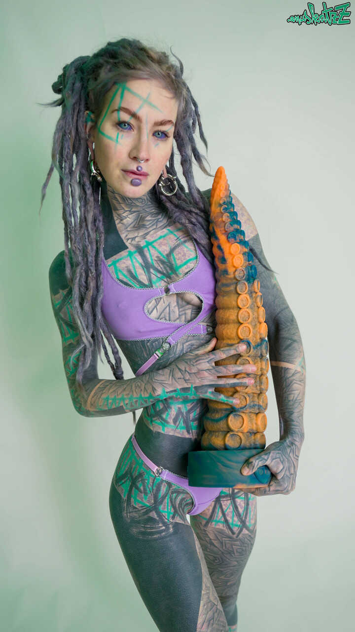 Heavily tattooed girl Anuskatzz holds a couple of taintacle toys in the nude while using her teeny tiny bikini and feet to tease with her huge dildo