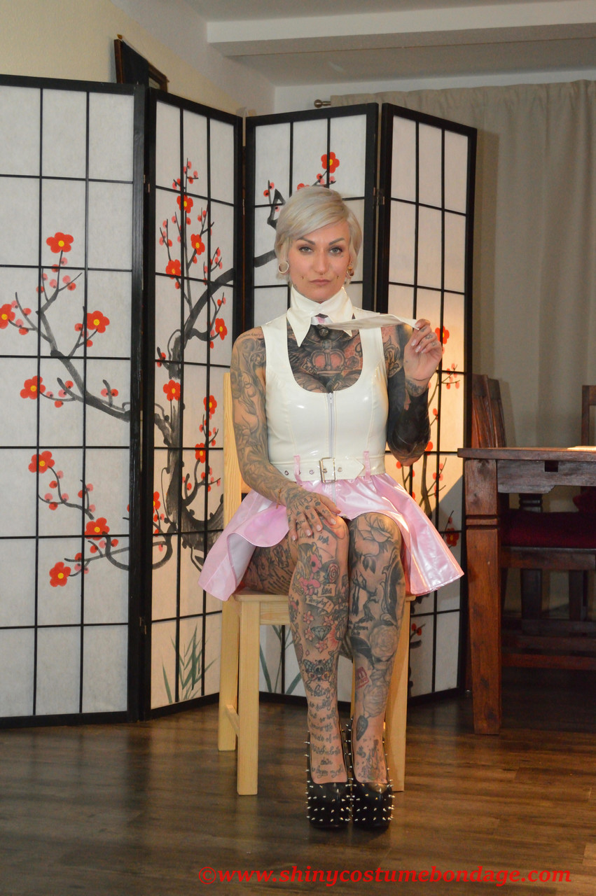 タトゥー入りプラチナブロンドのミス・フランシーヌ レインコート姿でラテックスドレスの上に