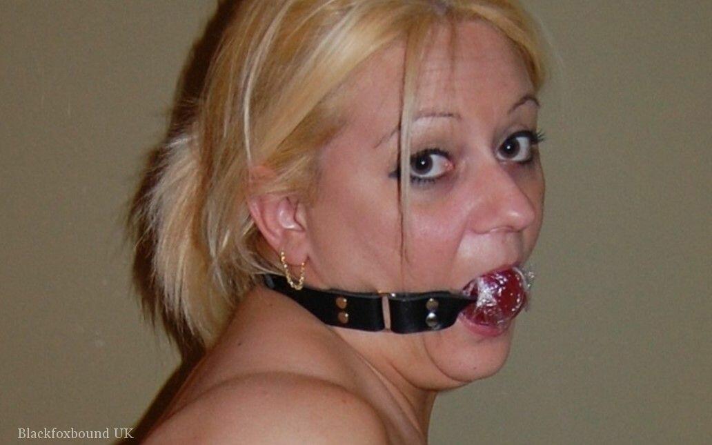 太った金髪の女性が手錠で縛られ青いホースの中でトップレスで口を塞がれている