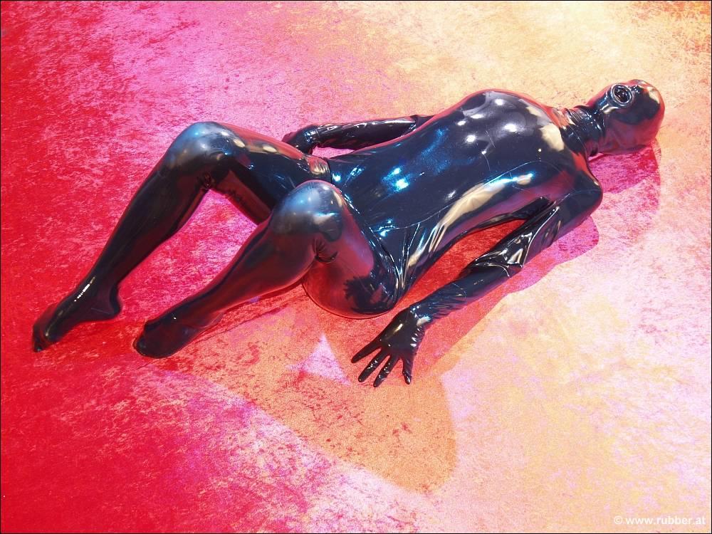 सिर से पांव तक लेटेक्स पोशाक में सोलो मॉडल, उसकी जांघों के बीच से खेल नलिकाएं बाहर निकल रही हैं