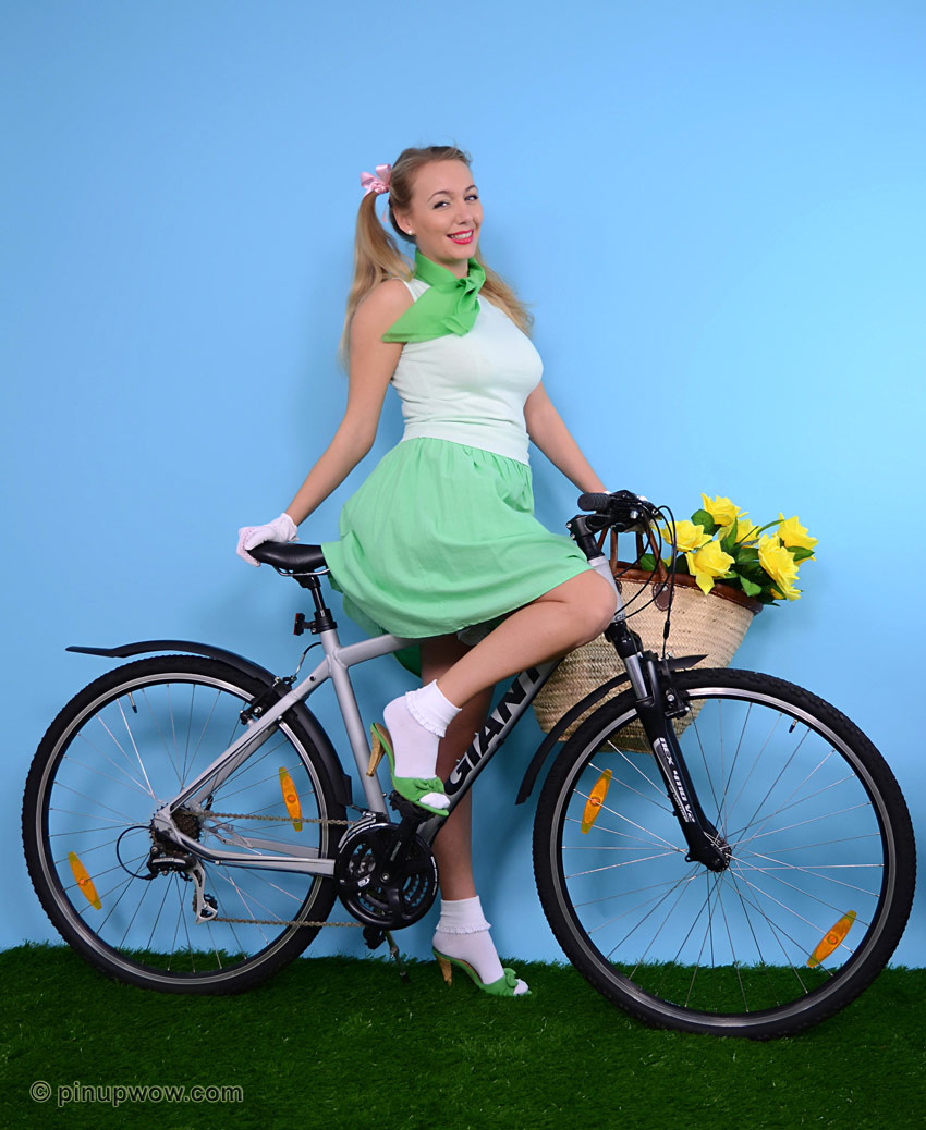 सुनहरे बालों वाली प्यारी लड़की साइकिल पर चढ़ी हुई है, सफेद दस्ताने और झालरदार पैंटी में अपने कसे हुए स्तन दिखा रही है