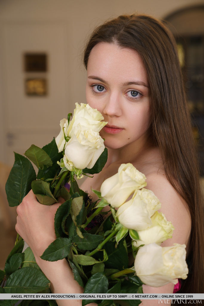 若い小柄な黒髪の天使が裸になる前に花を抱えている